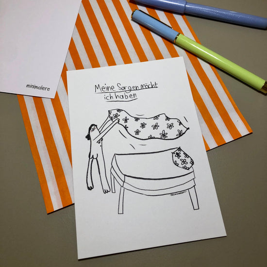 Eine Grußkarte mit der Aufschrift "Meine Sorgen möcht ich haben." liegt auf einer orange-weiß gestreiften Papiertüte, daneben liegen zwei Stifte.