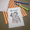 Eine Grußkarte mit der Aufschrift "Alles wird gut." liegt auf einer orange-weiß gestreiften Papiertüte, daneben liegen zwei Stifte.
