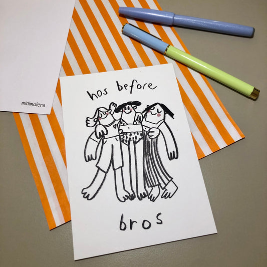 Eine Grußkarte mit der Aufschrift "hos before bros." liegt auf einer orange-weiß gestreiften Papiertüte, daneben liegen zwei Stifte.