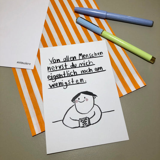 Eine Grußkarte mit der Aufschrift "Von allen Menschen nervst du mich eigentlich noch am wenigsten." liegt auf einer orange-weiß gestreiften Papiertüte, daneben liegen zwei Stifte.